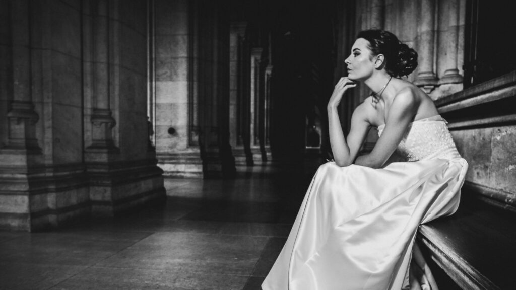 Zeitlos elegante Ballfotografie: Frau im weißen Ballkleid auf Steinbank